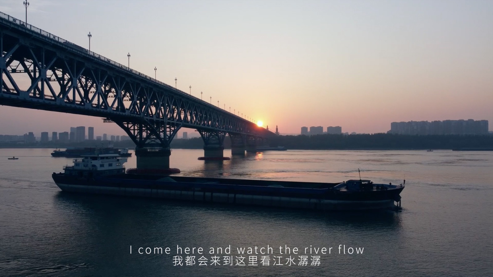 A cargo boat passing beneath the bridge at sunset