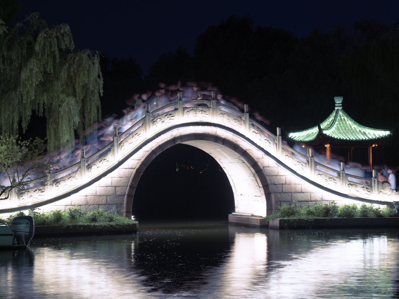 An illuminated arched bridge reflected in water