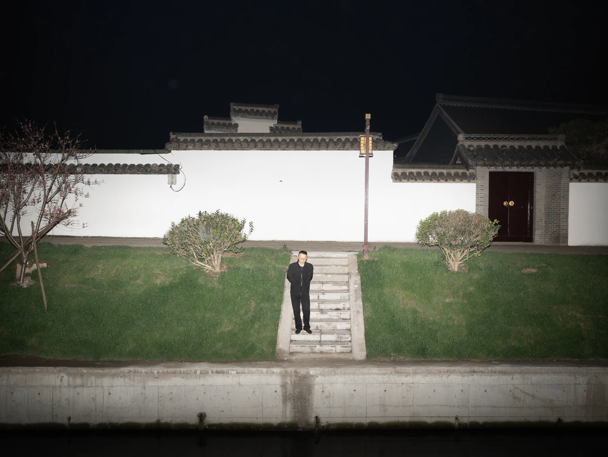 A person standing against a white exterior wall