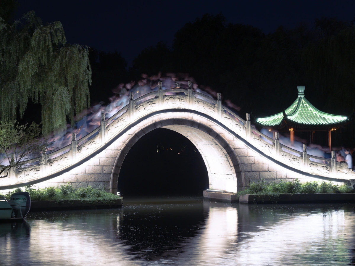 An illuminated arched bridge reflected in water