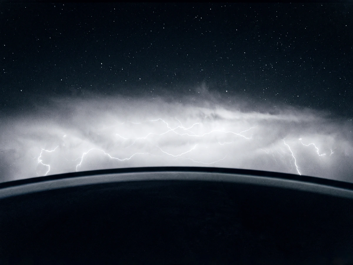 Lightning and clouds seen beyond a dark curved horizon
